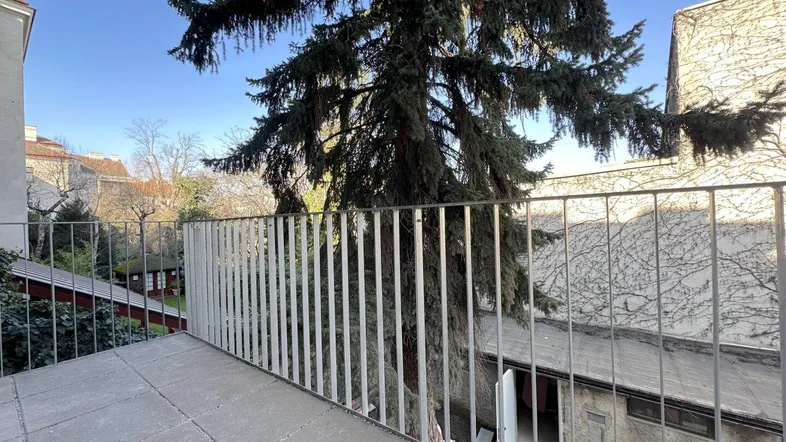 Geräumiger Balkon mit Fliesenboden und Metallgeländer, bietet einen ruhigen Blick ins Grüne und auf den Innenhof.