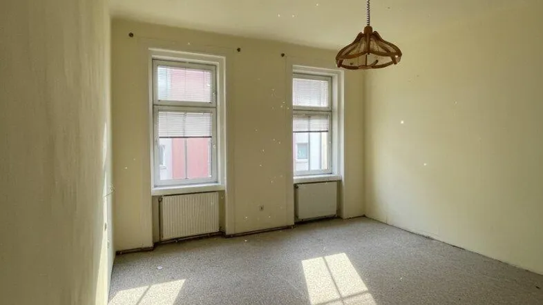 Helles, leeres Zimmer mit Teppichboden und zwei Fenstern, bereit zur individuellen Gestaltung.