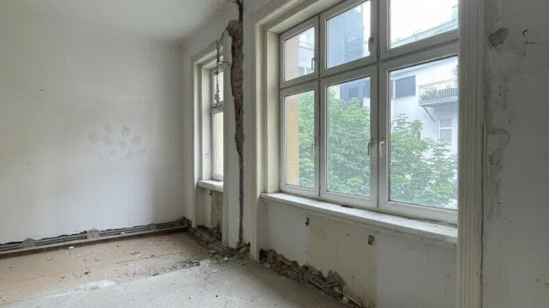 Unfertiger Raum mit großen Fenstern und freigelegten Wänden, bereit für den Ausbau.