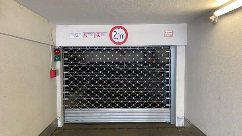 Eingang zu einer Tiefgarage mit geschlossenem Rolltor und einer Höhenbegrenzung von 2,1 Metern.