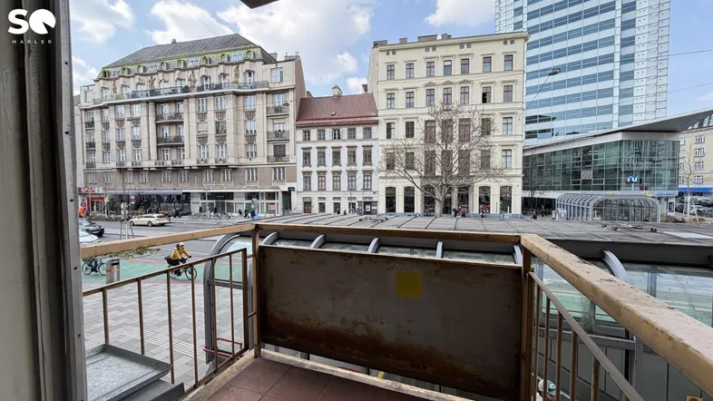 Blick vom kleinen Balkon auf die belebte Stadtstraße mit historischen Gebäuden und modernen Hochhäusern.