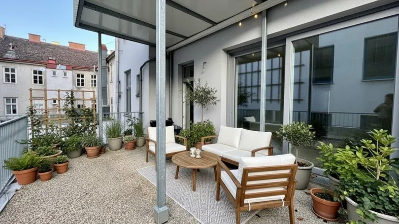 Gemütliche Terrasse mit Sitzgelegenheiten, vielen Pflanzen und Blick auf die umliegenden Gebäude.