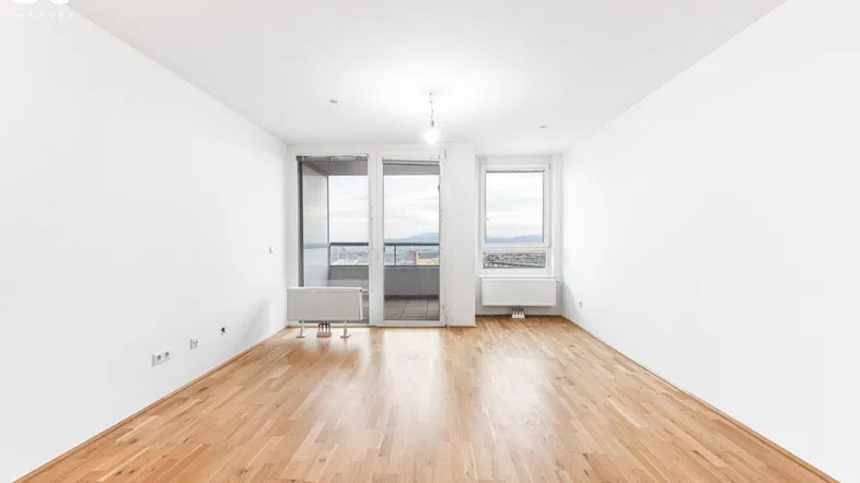 Helles Zimmer mit Parkettboden, weißen Wänden und Zugang zu einem Balkon.