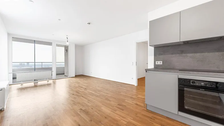 Helles Wohnzimmer mit Parkettboden und integrierter Küchenzeile, bietet Zugang zum Balkon und Stadtblick.