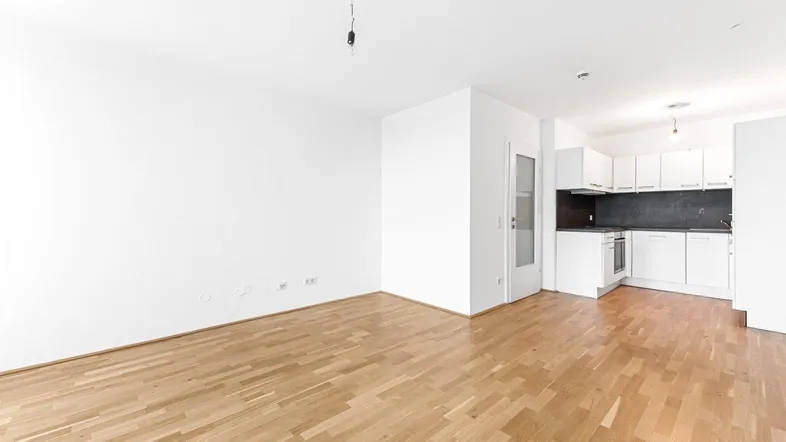 Helles Wohnzimmer mit offener Küche und Parkettboden, bereit zur individuellen Gestaltung.