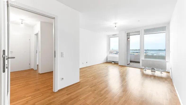 Helles Wohnzimmer mit Parkettboden, weißen Wänden und Zugang zu einem Balkon mit Stadtblick.