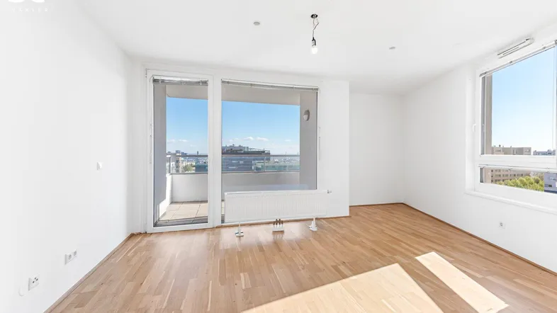 Helles, leeres Zimmer mit Parkettboden, großen Fenstern und Zugang zu einem Balkon mit Stadtblick.