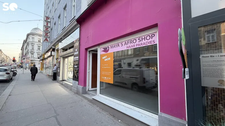 Blick auf die Straße mit einem Gebäude, das eine auffällige pinkfarbene Ladenfront und Passanten zeigt.