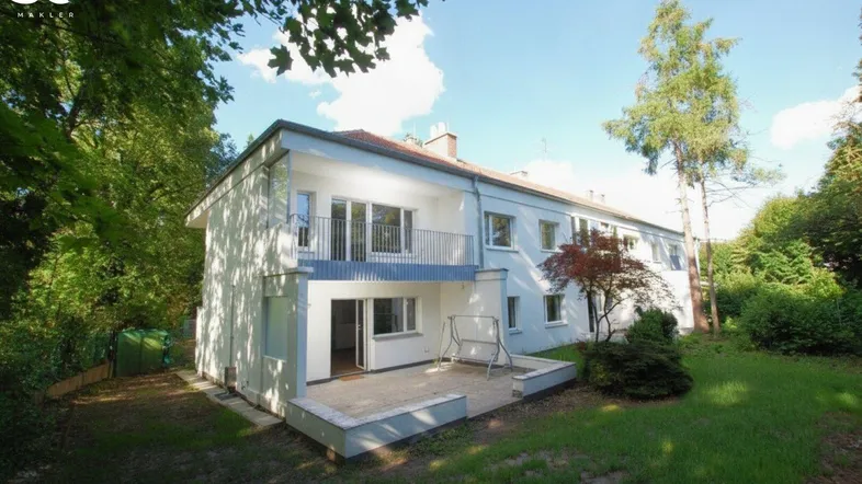 Hinteransicht des Hauses mit großem Garten, Terrasse und Balkon, umgeben von viel Grün.