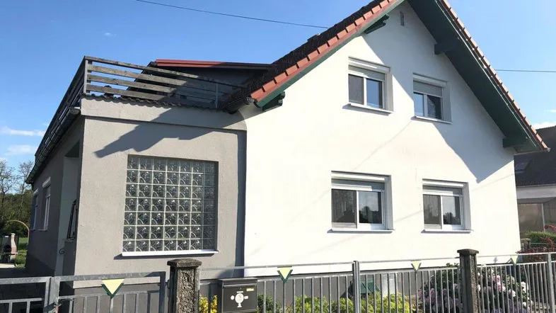 Weißes Einfamilienhaus mit rotem Ziegeldach und Glasbausteinen an der Fassade.