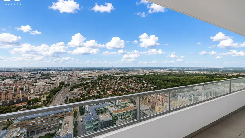 Weiter Blick über die Stadt und grüne Landschaften von einem modernen Balkon mit Glasgeländer.