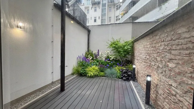 Schöne Terrasse mit Holzdeck und bepflanztem Blumenbeet, umgeben von Mauern für Privatsphäre.
