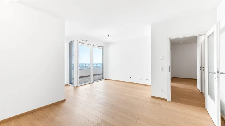 Helles, leeres Wohnzimmer mit Holzboden und Zugang zu einem Balkon mit Weitblick.