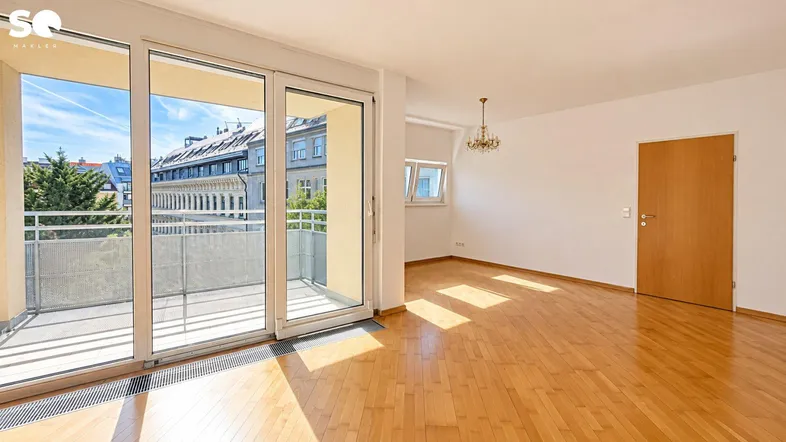 Helles Wohnzimmer mit Parkettboden, großen Schiebetüren und Zugang zu einem Balkon.