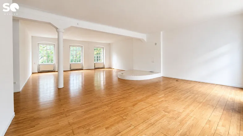 Großzügiger, heller Wohnraum mit Holzboden, hohen Decken und mehreren Fenstern, ideal für individuelle Gestaltung.