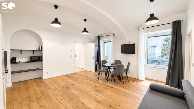 Helles Wohn- und Esszimmer mit Holzboden, Gewölbedecke und Blick auf die Straße.