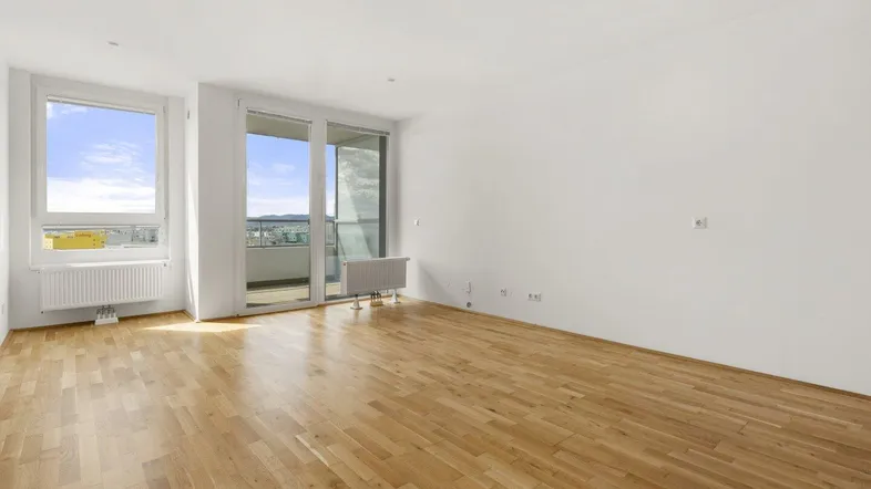 Helles Wohnzimmer mit Parkettboden, großen Fenstern und Zugang zum Balkon mit Stadtblick.