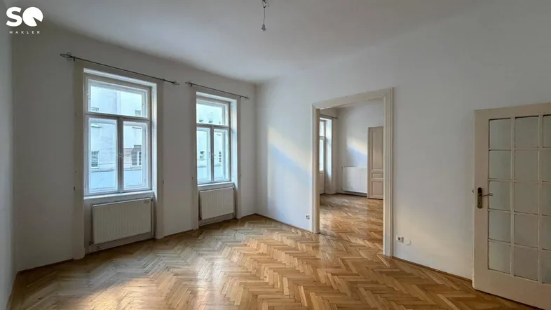 Helles Wohnzimmer mit klassischem Fischgrätparkett, weißen Wänden und hohen Fenstern für viel Tageslicht.