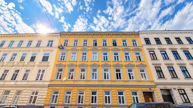 Historische Fassade eines Mehrfamilienhauses mit leuchtend gelbem Anstrich unter blauem Himmel.