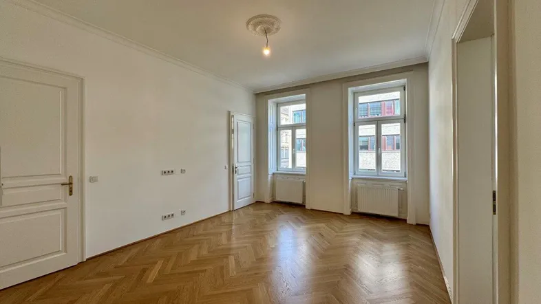 Helles Zimmer mit Fischgrätparkett, hohen Decken und Stuckelementen, bereit zur individuellen Gestaltung.