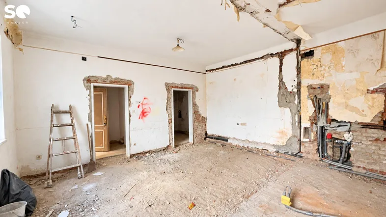 Innenraum im Rohzustand mit freigelegten Wänden, Betonboden und Renovierungsbedarf.