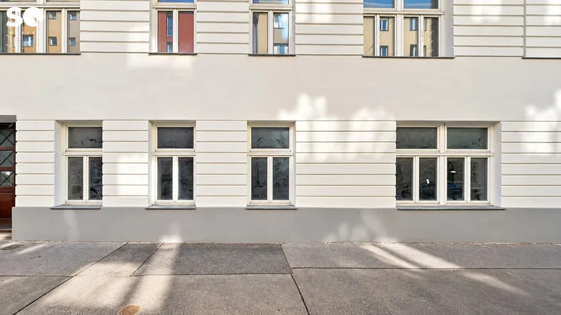 Fassade eines Altbaus mit mehreren Fenstern und einem Gehweg davor, gut erhalten.