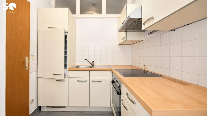 Kleine, funktionale Küche mit hellen Schränken, Holz-Arbeitsplatte und integrierten Geräten.