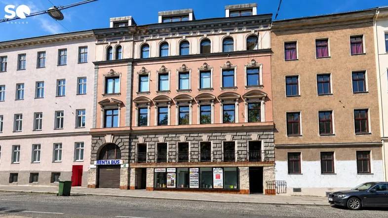Historisches Mehrfamilienhaus mit aufwendiger Fassade und Geschäftsräumen im Erdgeschoss an einer Stadtstraße.