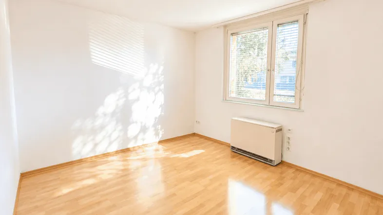 Helles Zimmer mit Parkettboden und großem Fenster, das viel Tageslicht hereinlässt.