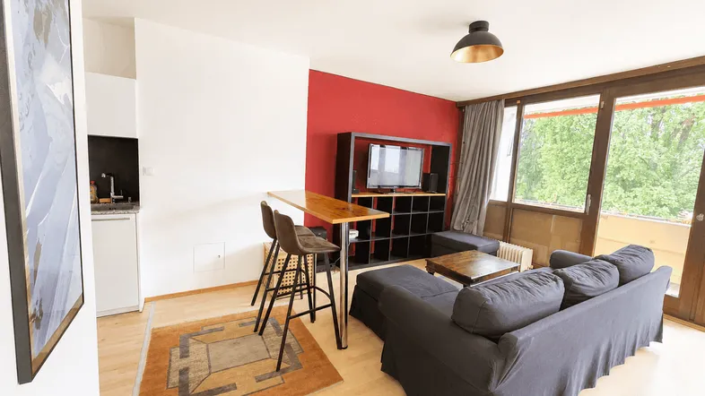 Helles Wohnzimmer mit roter Akzentwand, Holzboden und Zugang zum Balkon.