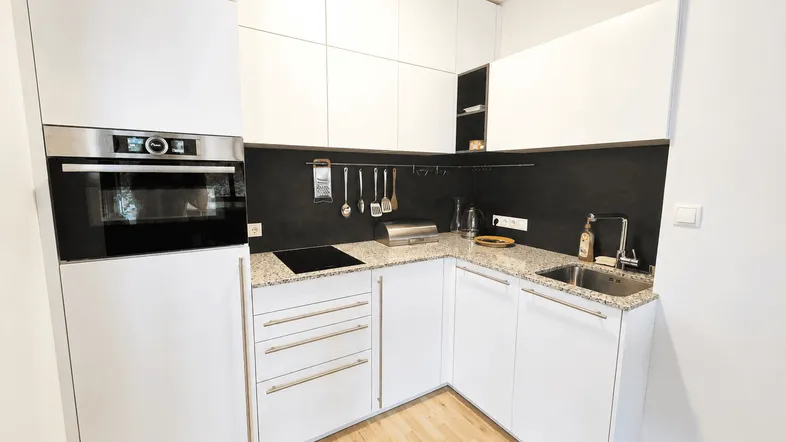 Moderne Einbauküche mit weißen Schränken, Granitarbeitsplatte und integrierten Geräten.