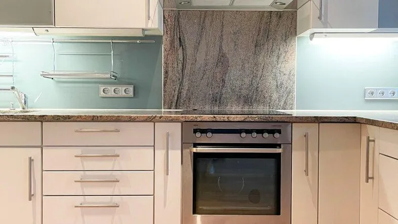 Moderne Einbauküche mit weißen Hochglanzfronten, Granitarbeitsplatte und integriertem Backofen.