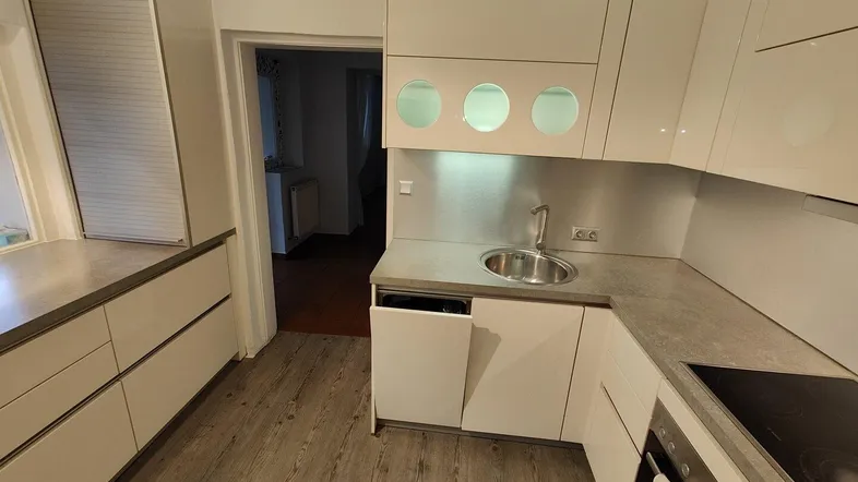 Moderne Küche mit weißen Hochglanzfronten, Spüle und Induktionskochfeld auf Laminatboden.