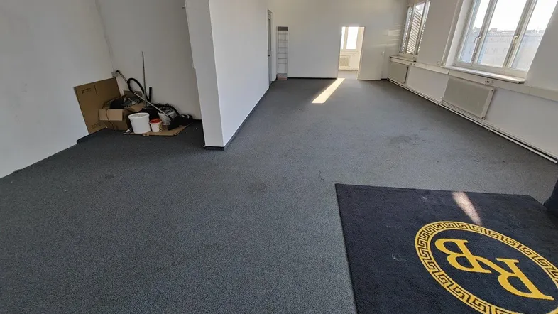 Geräumiges, leeres Büro mit grauem Teppichboden und großen Fenstern, bereit zur individuellen Gestaltung.