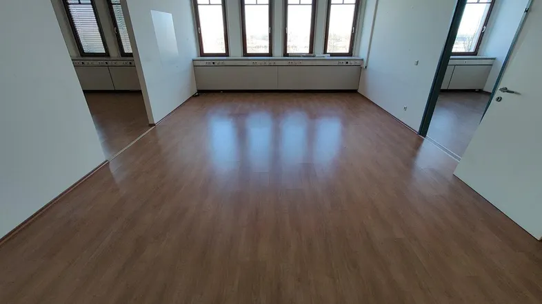 Geräumiges Büro mit hellem Laminatboden, vielen Fenstern und natürlichem Lichteinfall, bereit zur Nutzung.