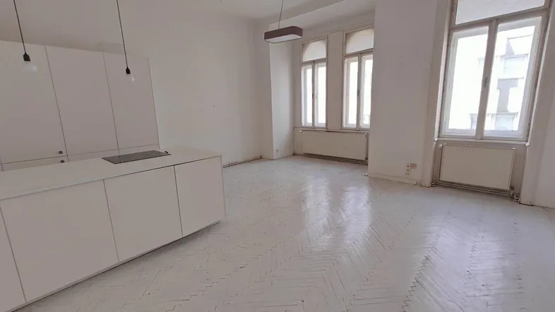 Heller, offener Wohnbereich mit integrierter Küche und Fischgrätparkett, bereit zur Renovierung.