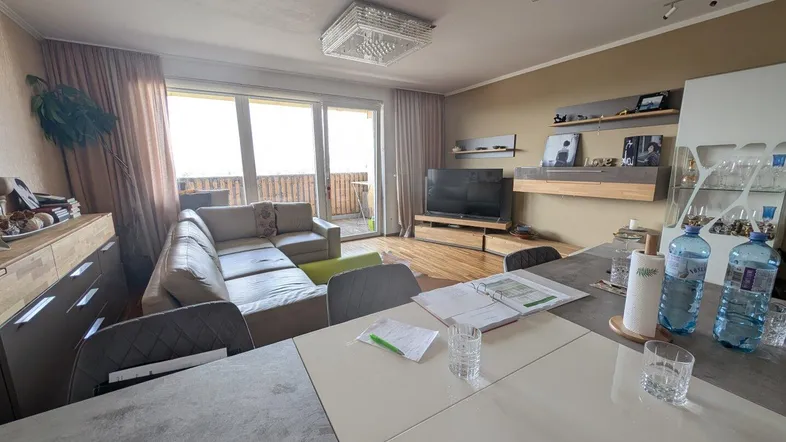 Geräumiger Wohn-Essbereich mit beigem Sofa, Holzboden und Zugang zu einem sonnigen Balkon.