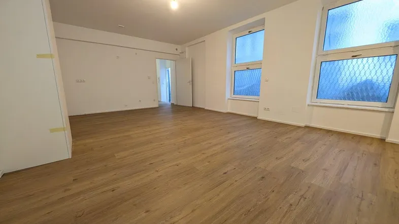 Geräumiges, leeres Zimmer mit hellem Laminatboden und mehreren Fenstern, bereit zur individuellen Gestaltung.