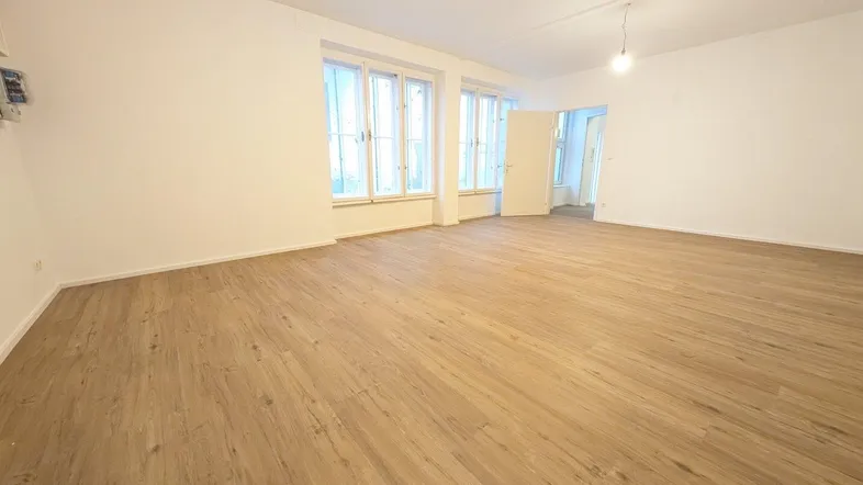 Helles, geräumiges Zimmer mit neuem Laminatboden und großen Fenstern, ideal als Wohnbereich.