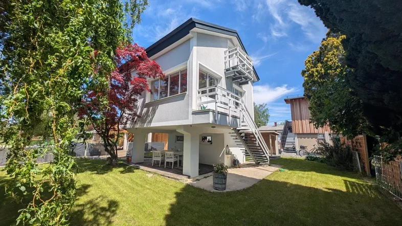 Modernes Haus mit großem Garten, Terrasse unter dem Gebäude und Außentreppe zum Obergeschoss.