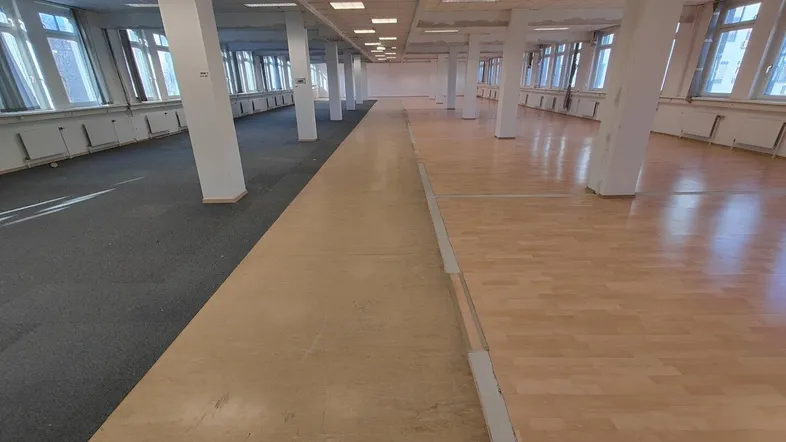 Großes, offenes Büro mit Säulen, einer Mischung aus Teppich- und Holzböden sowie vielen Fenstern.