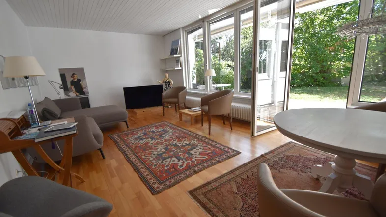 Helles Wohn- und Esszimmer mit Holzboden, großen Fenstern und Zugang zum Garten.