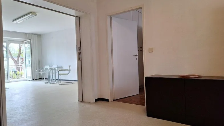 Heller Wohnbereich mit Zugang zum Balkon, ausgestattet mit einem dunklen Sideboard und hellen Wänden.