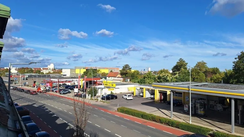 Weitläufiger Blick über eine städtische Straße mit Tankstelle und Gebäuden unter blauem Himmel.