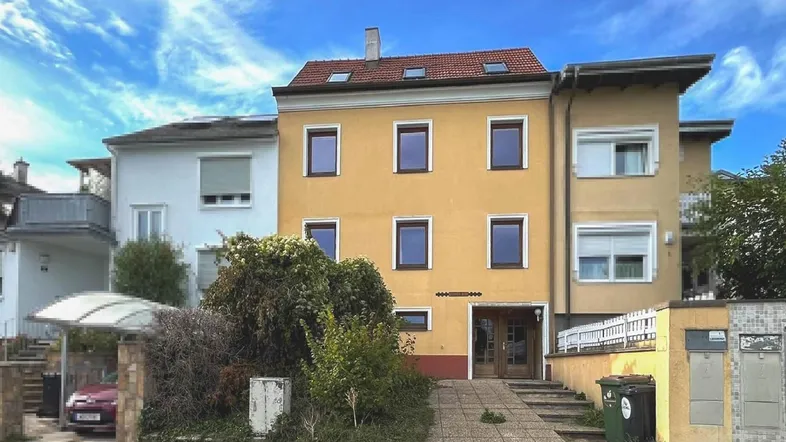 Gelbe Fassade eines Mehrfamilienhauses mit Eingangsbereich, Rampe und Carport.