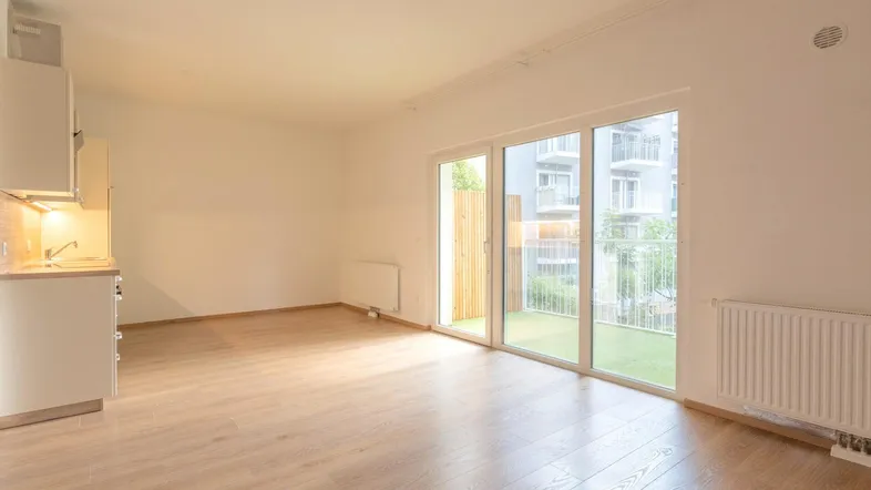 Helles Wohnzimmer mit Kochnische, Laminatboden und Zugang zu einem kleinen Balkon.