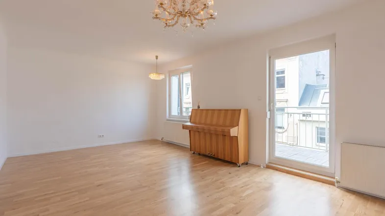 Helles, leeres Wohnzimmer mit Parkettboden, Kronleuchter und Zugang zu einem französischen Balkon.
