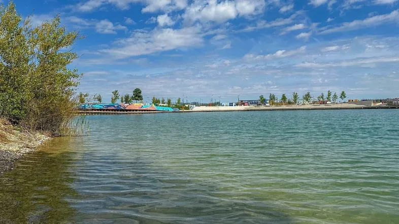 Weitläufiger Blick auf einen See oder Teich unter blauem Himmel mit leichter Bewölkung.