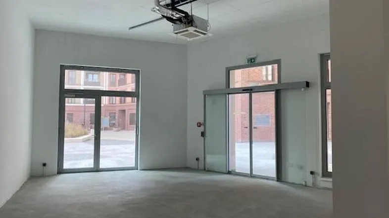Heller, leerer Gewerberaum mit großen Fenstern, Glastüren und Betonboden, ideal für verschiedene Nutzungen.