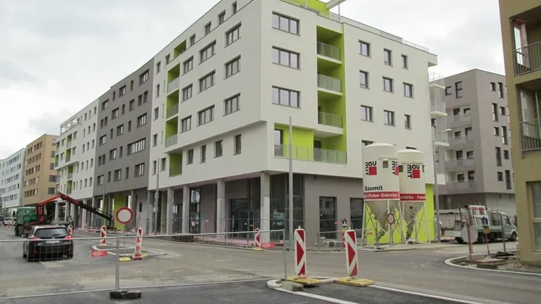 Modernes Mehrfamilienhaus in Neubaugebiet mit grünen Akzenten und Baustellenumgebung.